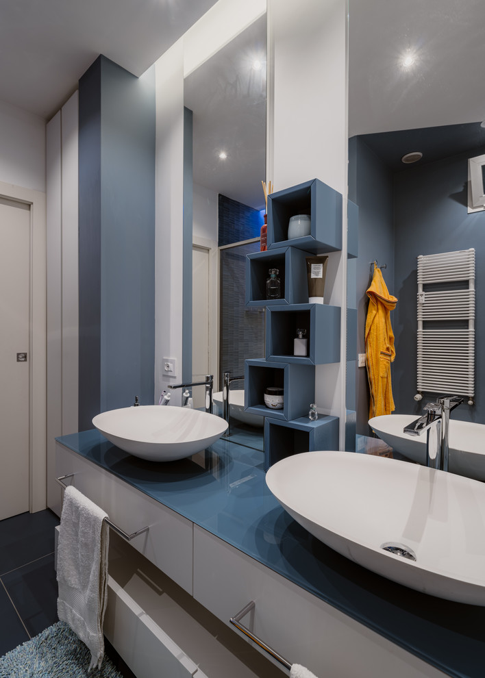 Пример оригинального дизайна: маленькая ванная комната в стиле модернизм с плоскими фасадами, бирюзовыми фасадами, душем в нише, раздельным унитазом, синей плиткой, керамогранитной плиткой, разноцветными стенами, полом из керамогранита, душевой кабиной, настольной раковиной, стеклянной столешницей, синим полом, душем с раздвижными дверями и синей столешницей для на участке и в саду