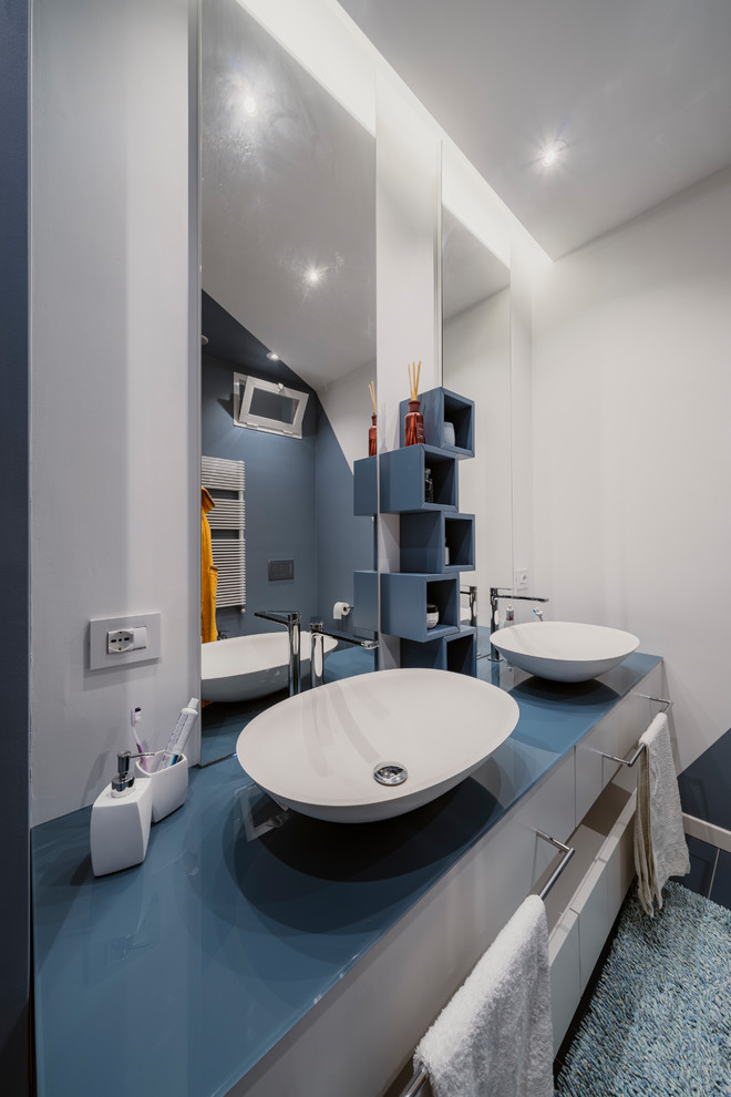 Modern inredning av ett litet blå blått badrum med dusch, med släta luckor, turkosa skåp, en dusch i en alkov, en toalettstol med separat cisternkåpa, blå kakel, porslinskakel, flerfärgade väggar, klinkergolv i porslin, ett fristående handfat, bänkskiva i glas, blått golv och dusch med skjutdörr