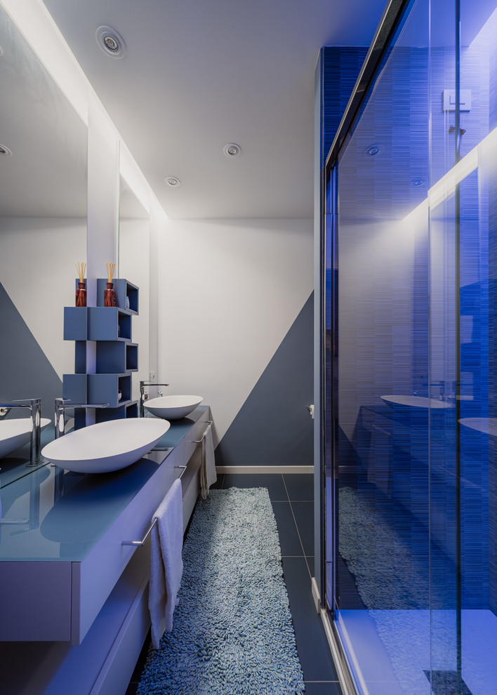 Пример оригинального дизайна: маленькая ванная комната в стиле модернизм с плоскими фасадами, бирюзовыми фасадами, душем в нише, раздельным унитазом, синей плиткой, керамогранитной плиткой, разноцветными стенами, полом из керамогранита, душевой кабиной, настольной раковиной, стеклянной столешницей, синим полом, душем с раздвижными дверями и синей столешницей для на участке и в саду