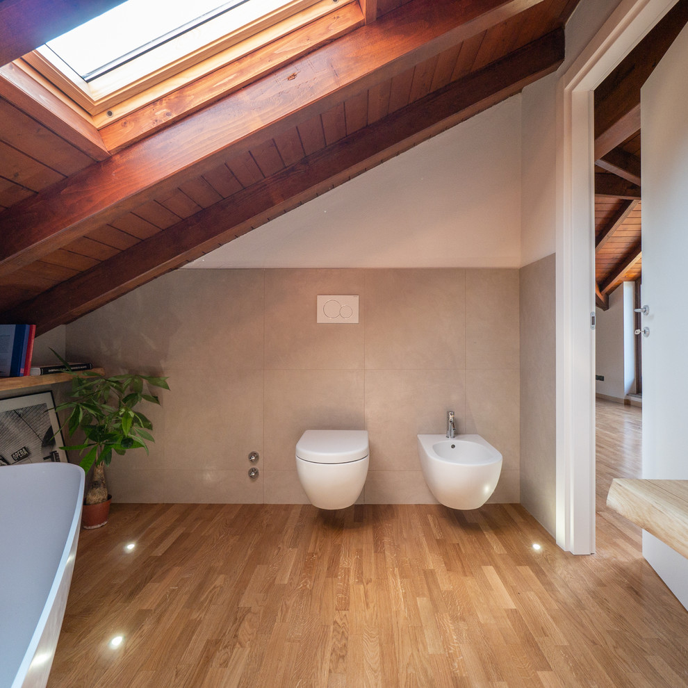 Bild på ett mellanstort medelhavsstil en-suite badrum, med skåp i ljust trä, ett fristående badkar, en vägghängd toalettstol, beige kakel, porslinskakel, vita väggar, ljust trägolv, ett fristående handfat och träbänkskiva