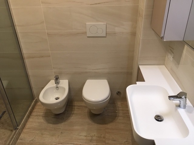Small contemporary shower room bathroom in Milan with flat-panel cabinets, beige cabinets, a double shower, a wall mounted toilet, beige tiles, porcelain tiles, beige walls, porcelain flooring, an integrated sink, quartz worktops, beige floors and a sliding door.