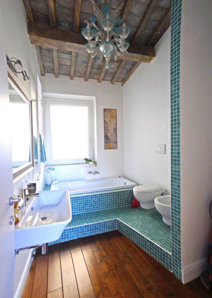 Idée de décoration pour une salle de bain principale méditerranéenne avec une baignoire posée, un carrelage vert, un carrelage bleu, un lavabo suspendu, un bidet, un mur blanc, parquet foncé et un sol marron.