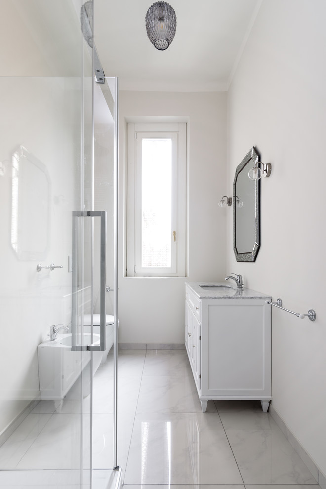 На фото: узкая и длинная ванная комната среднего размера в стиле неоклассика (современная классика) с белыми фасадами, инсталляцией, белыми стенами, душевой кабиной, врезной раковиной, мраморной столешницей и душем с раздвижными дверями