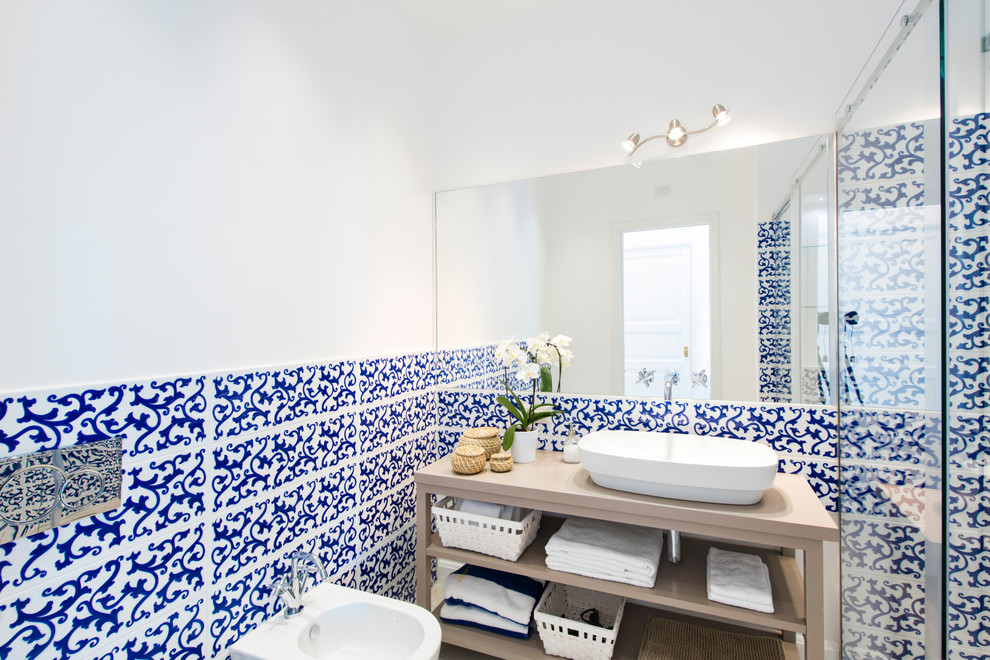 Inredning av ett medelhavsstil badrum med dusch, med öppna hyllor, skåp i ljust trä, en dusch i en alkov, blå kakel, flerfärgad kakel, vit kakel, vita väggar, ett fristående handfat och träbänkskiva