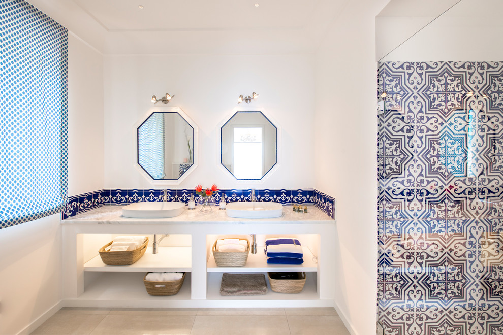 Maritimes Badezimmer mit offenen Schränken, weißen Schränken, weißen Fliesen, blauen Fliesen, weißer Wandfarbe, Aufsatzwaschbecken, beigem Boden und grauer Waschtischplatte in Rom