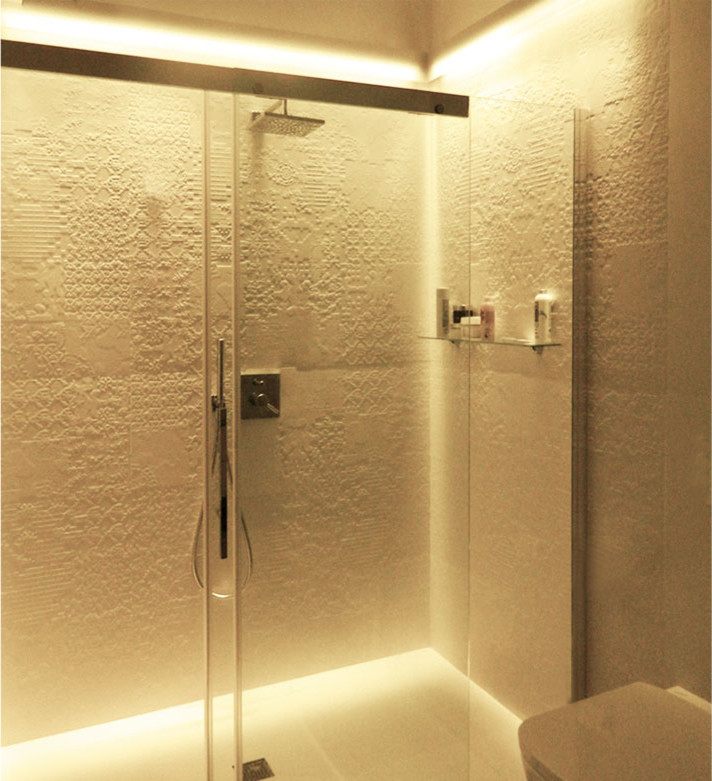 Bild på ett stort funkis badrum med dusch, med en kantlös dusch, en vägghängd toalettstol, porslinskakel, vita väggar, klinkergolv i porslin, ett avlångt handfat, vitt golv och dusch med skjutdörr