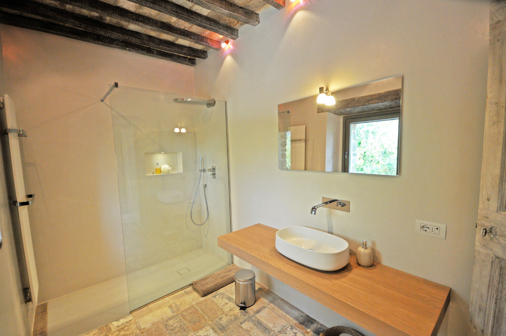 Idéer för ett mellanstort rustikt badrum med dusch, med skåp i ljust trä, en kantlös dusch, en toalettstol med separat cisternkåpa, beige väggar, klinkergolv i terrakotta, ett fristående handfat, träbänkskiva, flerfärgat golv och med dusch som är öppen