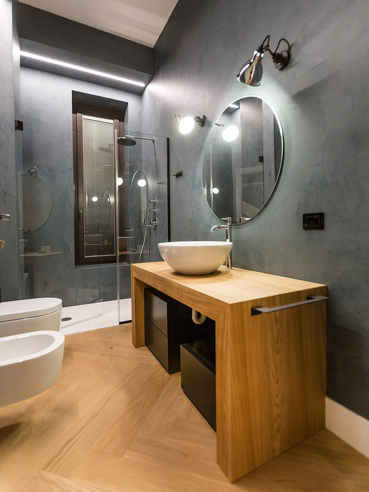 Foto på ett mellanstort funkis badrum, med släta luckor, grå väggar, ljust trägolv, ett fristående handfat, träbänkskiva, beiget golv, svarta skåp, en dusch i en alkov, en bidé, svart kakel, cementkakel och dusch med gångjärnsdörr