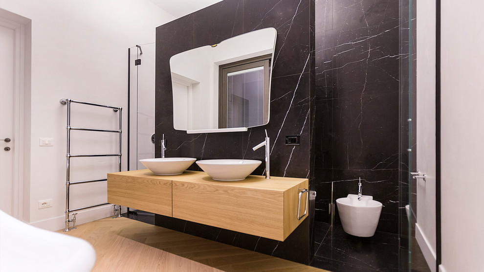 Immagine di una stanza da bagno minimalista di medie dimensioni con ante lisce, ante in legno chiaro, WC a due pezzi, piastrelle nere, piastrelle di marmo, pareti nere, pavimento in marmo, lavabo a bacinella, top in legno e pavimento beige