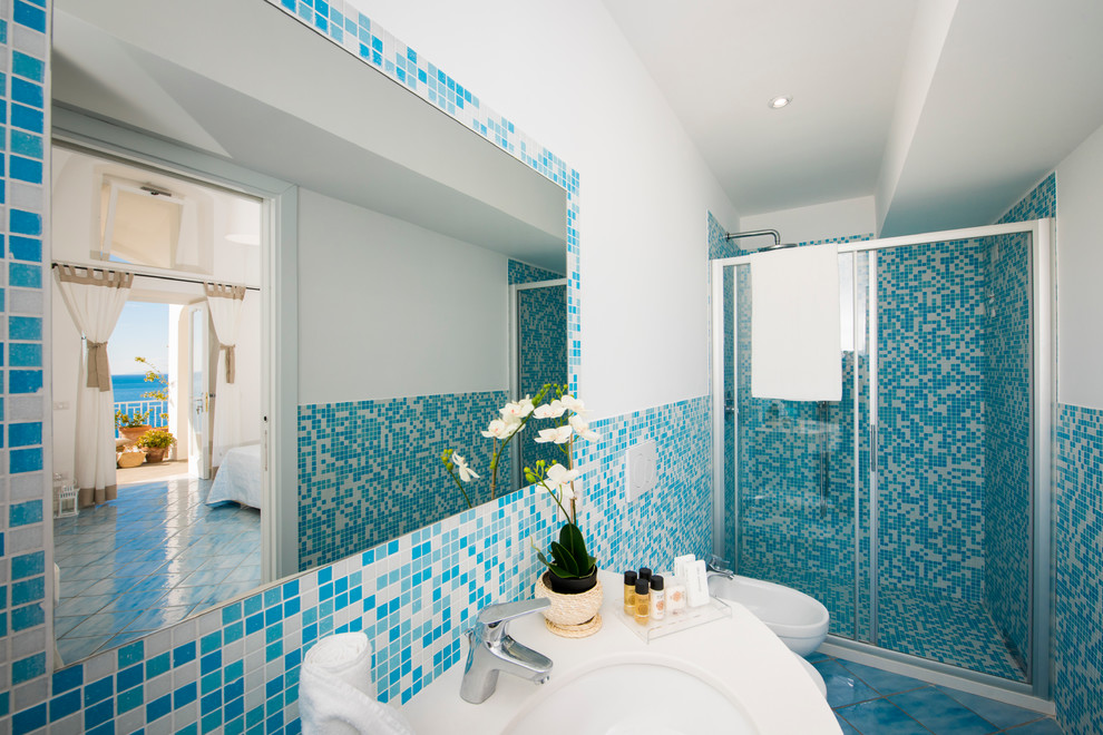 Cette image montre une salle d'eau méditerranéenne de taille moyenne avec WC à poser, des carreaux en terre cuite, un mur blanc, tomettes au sol, un placard à porte plane, des portes de placard blanches, une douche à l'italienne, un carrelage bleu, un lavabo suspendu, un plan de toilette en marbre, un sol turquoise, une cabine de douche à porte coulissante, un plan de toilette blanc, du carrelage bicolore, meuble double vasque, meuble-lavabo suspendu et un plafond décaissé.