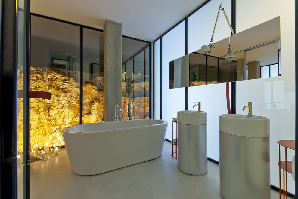 Cette image montre une grande salle de bain principale design avec une baignoire indépendante, sol en béton ciré, un lavabo de ferme et un placard à porte plane.