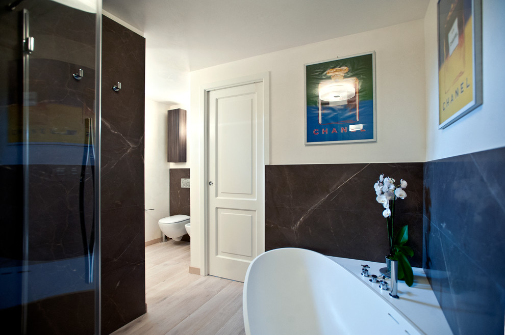 Cette photo montre une salle de bain moderne en bois foncé avec un placard à porte plane, une baignoire posée, une douche d'angle, WC suspendus, du carrelage en marbre, parquet foncé et une cabine de douche à porte battante.