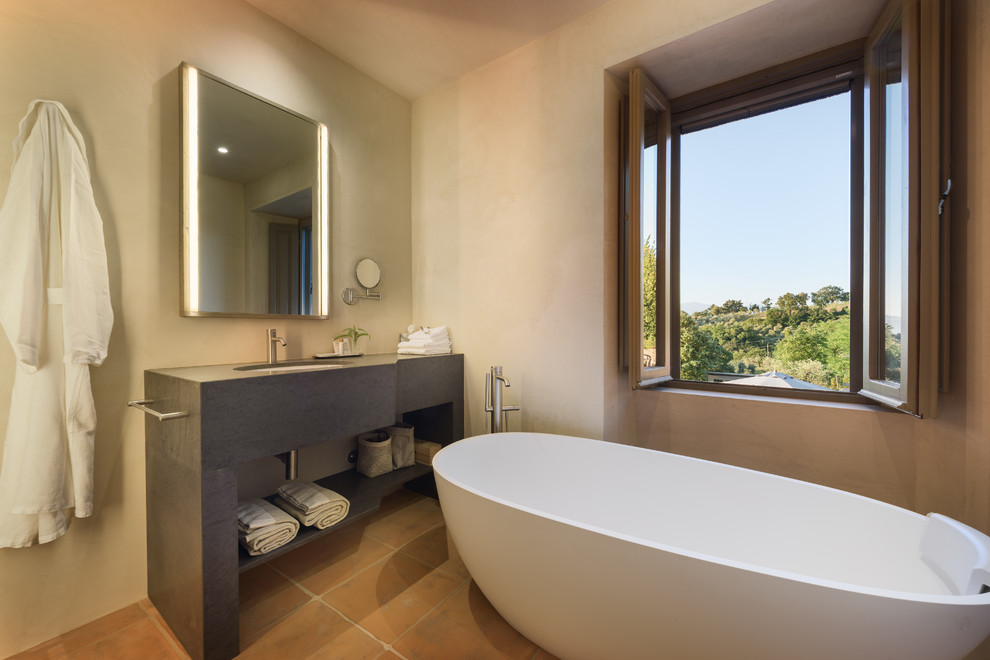 Mediterranes Badezimmer mit grauen Schränken, freistehender Badewanne, beiger Wandfarbe, Terrakottaboden, Unterbauwaschbecken, braunem Boden und grauer Waschtischplatte in Florenz