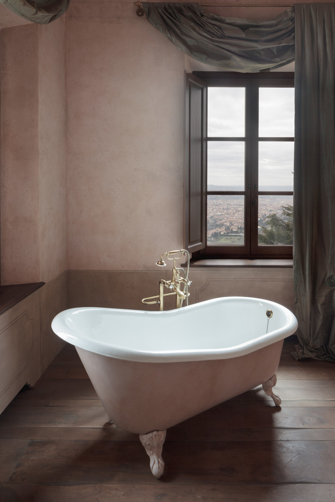 Idée de décoration pour une salle de bain tradition de taille moyenne avec une baignoire sur pieds, un mur rose, un sol en bois brun et un sol marron.