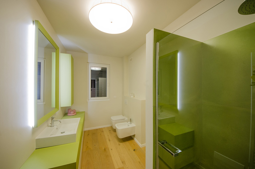 Modern inredning av ett mellanstort grön grönt badrum med dusch, med släta luckor, gröna skåp, en kantlös dusch, en vägghängd toalettstol, grön kakel, cementkakel, vita väggar, målat trägolv, ett fristående handfat, träbänkskiva, brunt golv och dusch med skjutdörr