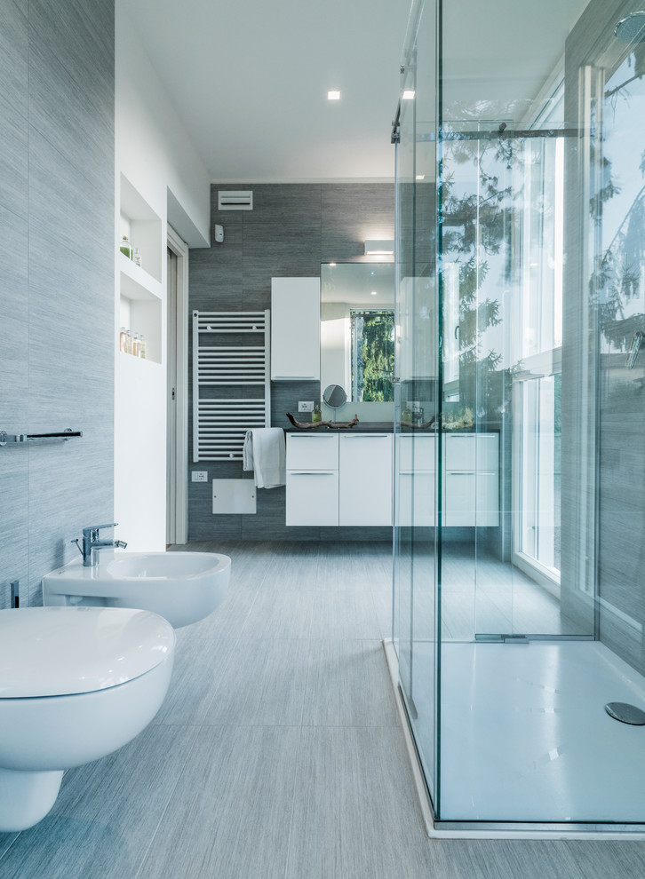 Bild på ett stort funkis badrum med dusch, med släta luckor, vita skåp, en kantlös dusch, en vägghängd toalettstol, vita väggar och klinkergolv i porslin