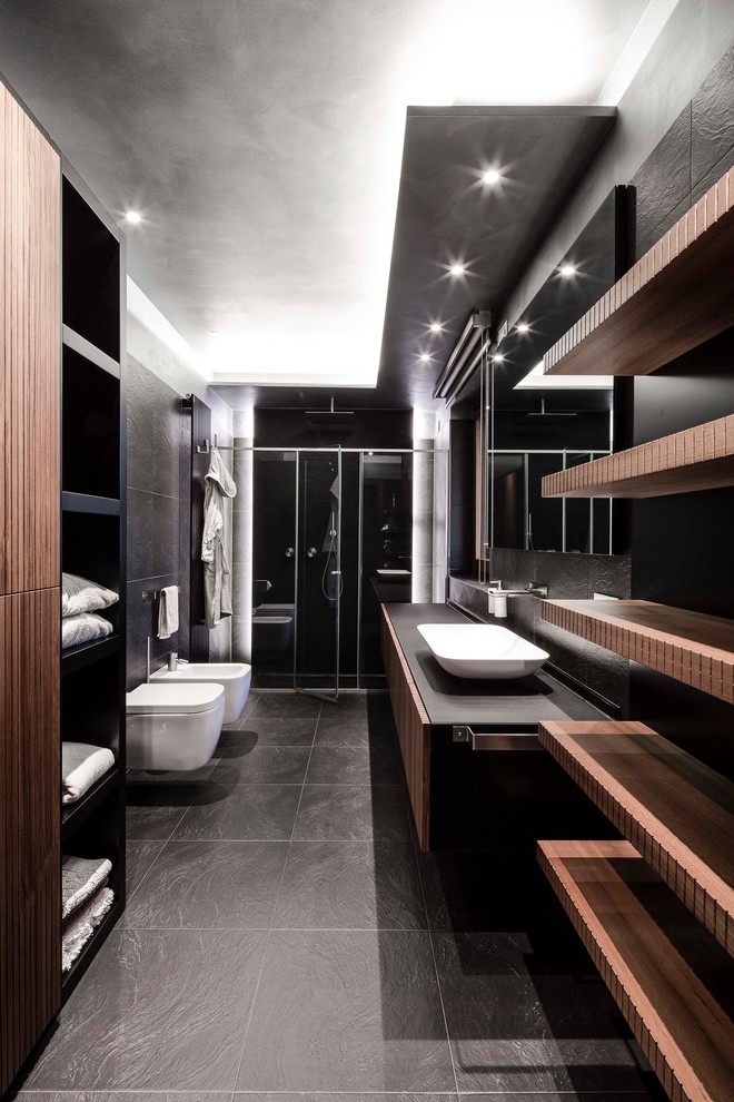 Diseño de cuarto de baño contemporáneo con armarios con paneles lisos, puertas de armario de madera oscura, ducha empotrada, sanitario de pared, baldosas y/o azulejos negros, aseo y ducha, lavabo sobreencimera y ducha con puerta con bisagras