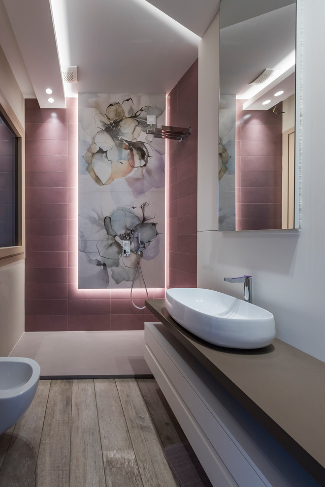 Modernes Duschbad mit offenen Schränken, offener Dusche, Bidet, rosa Fliesen, weißer Wandfarbe, braunem Holzboden, Aufsatzwaschbecken, grauem Boden, offener Dusche und grauer Waschtischplatte in Sonstige