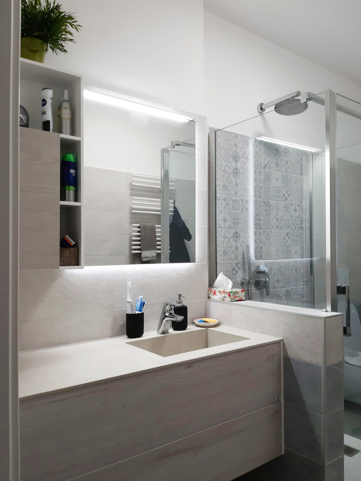 Пример оригинального дизайна: ванная комната среднего размера в современном стиле с плоскими фасадами, бежевыми фасадами, открытым душем, раздельным унитазом, серой плиткой, керамогранитной плиткой, белыми стенами, полом из керамогранита, душевой кабиной, накладной раковиной, столешницей из искусственного камня, серым полом, душем с распашными дверями, белой столешницей, тумбой под одну раковину и встроенной тумбой