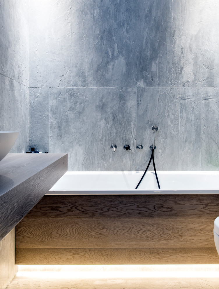 Exempel på ett litet modernt en-suite badrum, med skåp i ljust trä, ett platsbyggt badkar, en vägghängd toalettstol, grå kakel, stenhäll, grå väggar, målat trägolv, ett fristående handfat, träbänkskiva och beiget golv