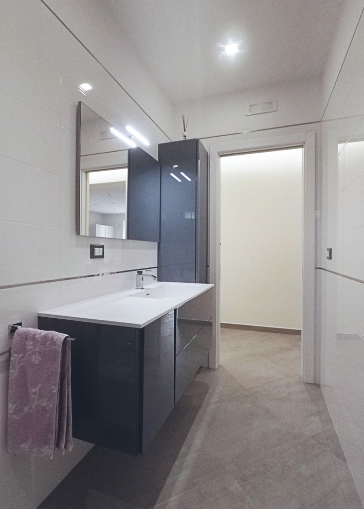 Idéer för mellanstora funkis vitt badrum med dusch, med släta luckor, grå skåp, en kantlös dusch, en toalettstol med separat cisternkåpa, vit kakel, porslinskakel, vita väggar, klinkergolv i porslin, ett integrerad handfat, bänkskiva i akrylsten, grått golv och dusch med skjutdörr