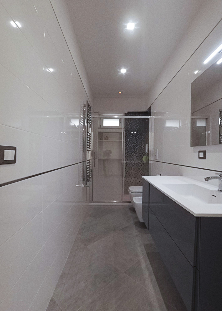 Foto på ett mellanstort funkis vit badrum med dusch, med släta luckor, grå skåp, en kantlös dusch, en toalettstol med separat cisternkåpa, vit kakel, porslinskakel, vita väggar, klinkergolv i porslin, ett integrerad handfat, bänkskiva i akrylsten, grått golv och dusch med skjutdörr