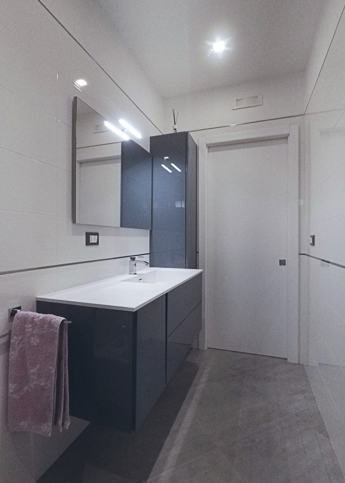 Inredning av ett modernt mellanstort vit vitt badrum med dusch, med släta luckor, grå skåp, en kantlös dusch, en toalettstol med separat cisternkåpa, vit kakel, porslinskakel, vita väggar, klinkergolv i porslin, ett integrerad handfat, bänkskiva i akrylsten, grått golv och dusch med skjutdörr