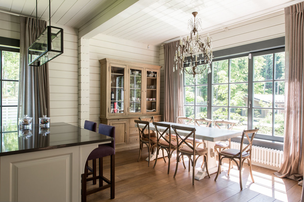 Réalisation d'une salle à manger ouverte sur la cuisine champêtre avec un mur blanc et un sol en bois brun.