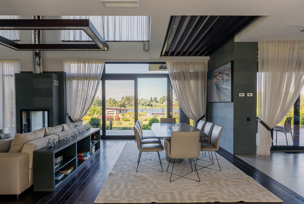 Idée de décoration pour une salle à manger ouverte sur le salon design avec un mur gris, une cheminée double-face, un manteau de cheminée en pierre et un sol marron.
