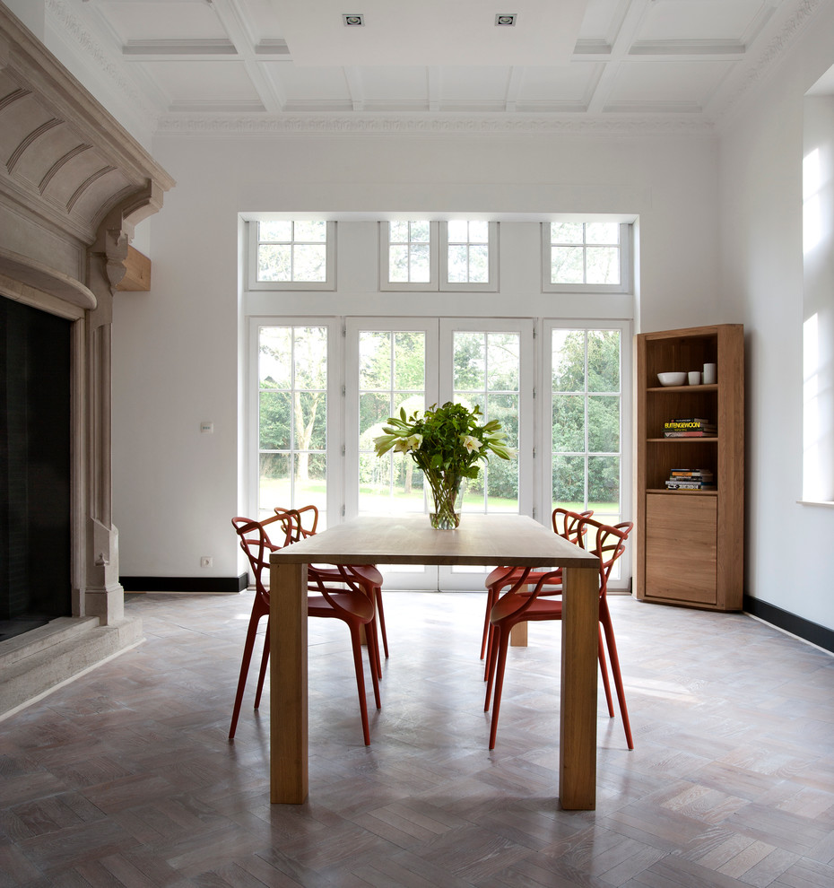 На фото: отдельная столовая в скандинавском стиле с белыми стенами, светлым паркетным полом и стандартным камином с