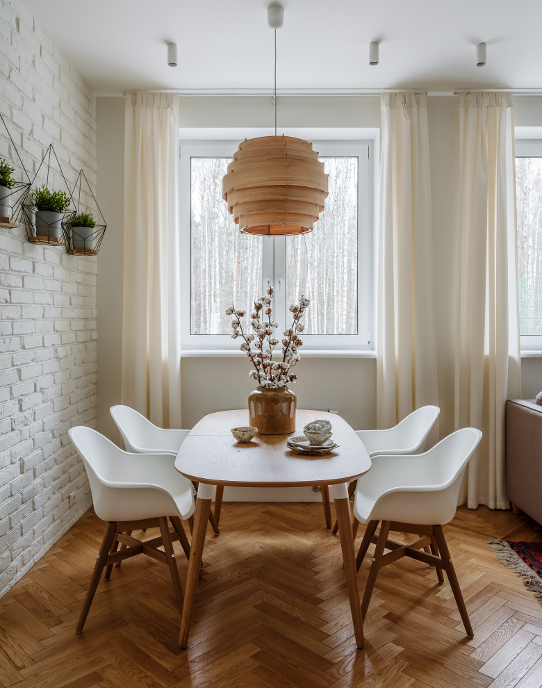 Cette image montre une salle à manger nordique avec un mur blanc, un sol en bois brun, un sol marron et un mur en parement de brique.