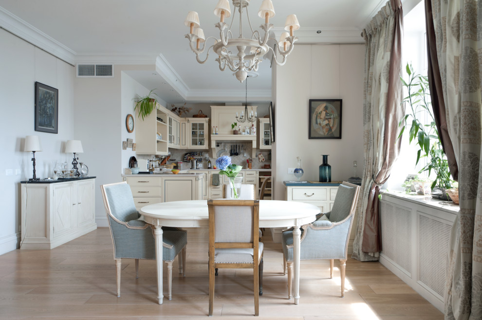 Réalisation d'une salle à manger ouverte sur la cuisine tradition avec un mur blanc et parquet clair.