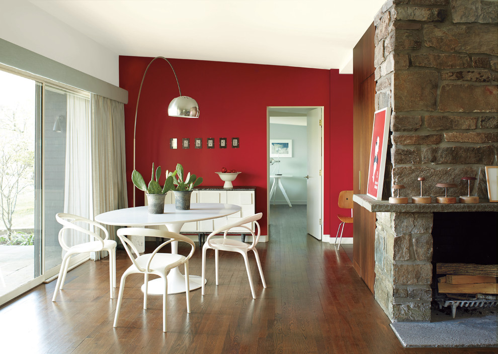 Idées déco pour une salle à manger ouverte sur le salon bord de mer avec un mur rouge, parquet foncé, une cheminée standard, un manteau de cheminée en pierre, un sol marron et éclairage.