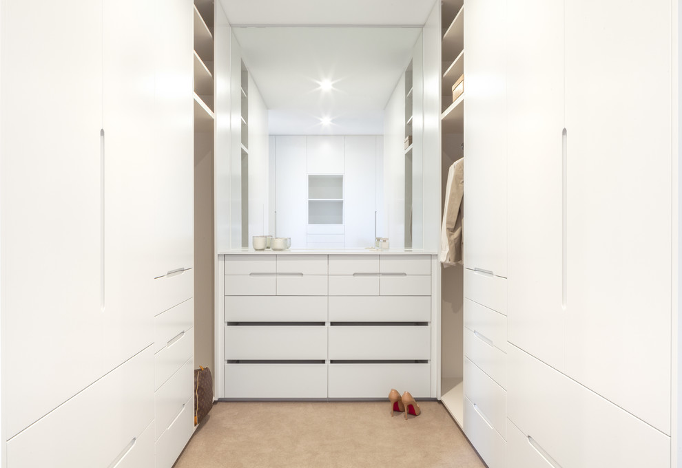 Réalisation d'un dressing minimaliste de taille moyenne avec des portes de placard blanches, moquette et un sol beige.