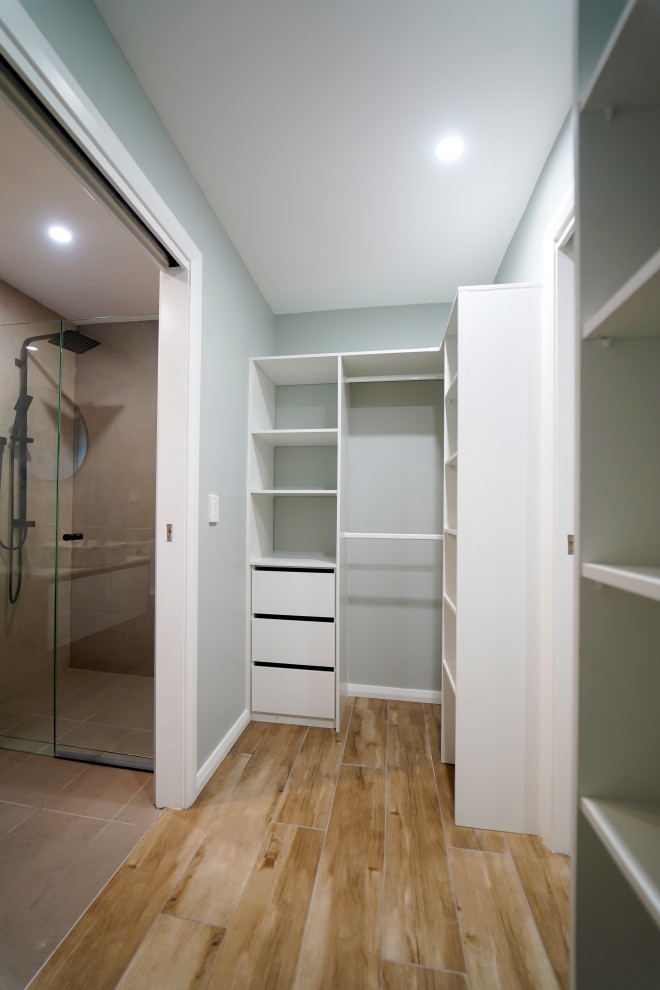 На фото: гардеробная комната среднего размера, унисекс в современном стиле с полом из ламината и бежевым полом с