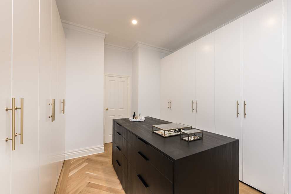 Cette photo montre un dressing room tendance de taille moyenne et neutre avec un placard à porte plane, des portes de placard noires, parquet clair et un sol marron.