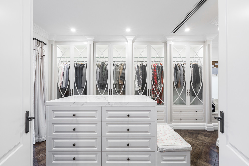 Diseño de armario vestidor actual grande con armarios tipo vitrina, puertas de armario blancas y suelo de madera oscura