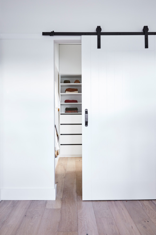 Minimalistisk inredning av ett walk-in-closet för könsneutrala, med vita skåp, ljust trägolv och brunt golv