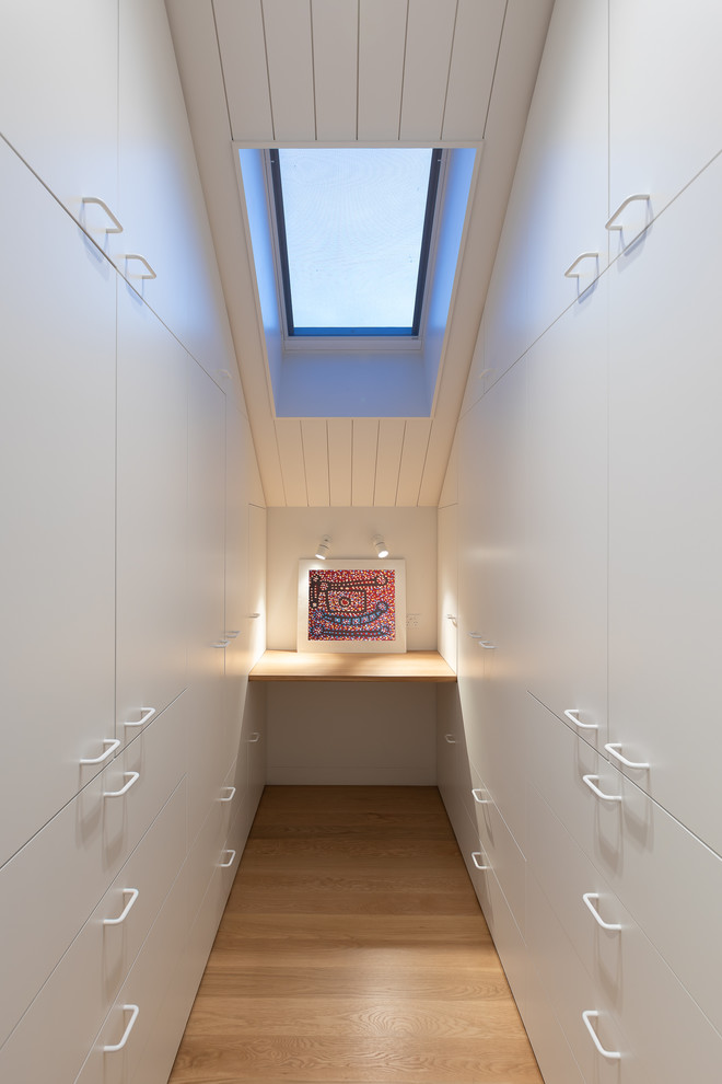 Idéer för att renovera ett mellanstort funkis walk-in-closet för könsneutrala, med luckor med infälld panel, vita skåp, ljust trägolv och brunt golv