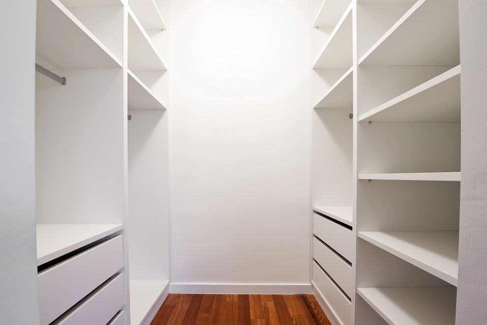 Modelo de armario vestidor unisex moderno de tamaño medio con suelo de madera en tonos medios, armarios abiertos y puertas de armario blancas