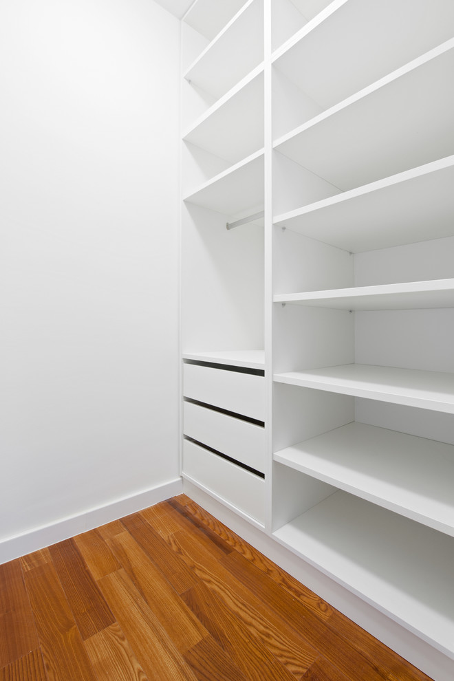 Imagen de armario vestidor unisex moderno de tamaño medio con suelo de madera en tonos medios, armarios abiertos y puertas de armario blancas