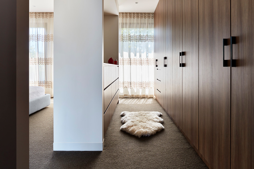 This is an example of a large contemporary gender neutral walk-in wardrobe in Melbourne with flat-panel cabinets, medium wood cabinets, carpet and brown floors.