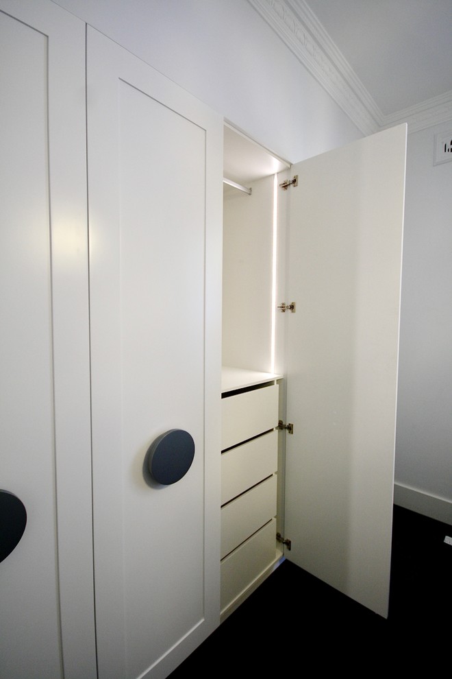 Aménagement d'un grand placard dressing classique neutre avec un placard à porte shaker, des portes de placard blanches, moquette et un sol noir.