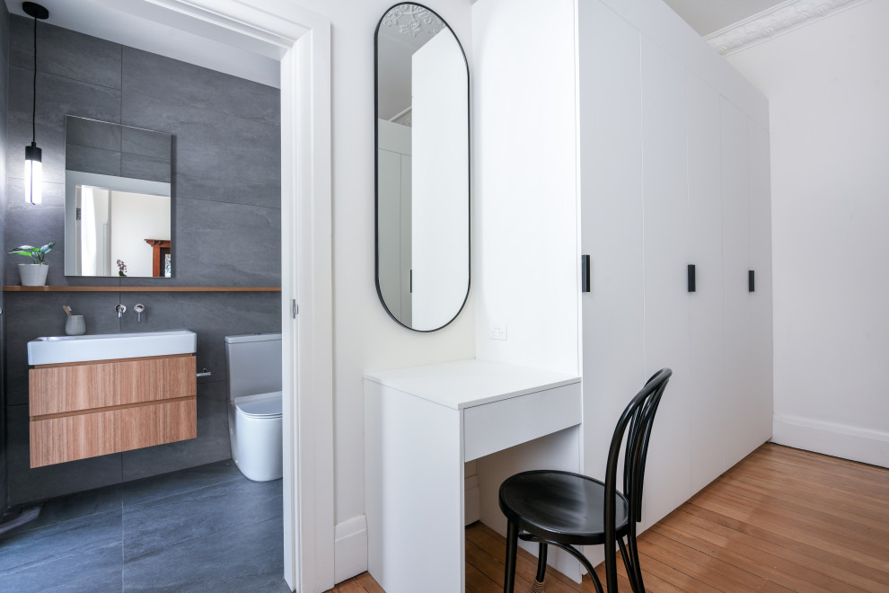 Imagen de armario vestidor unisex minimalista grande con armarios con paneles lisos, puertas de armario blancas, suelo de madera en tonos medios y suelo marrón