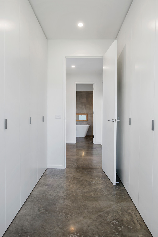 Ejemplo de armario vestidor unisex contemporáneo grande con puertas de armario blancas, suelo de cemento, armarios con paneles lisos, suelo gris y bandeja