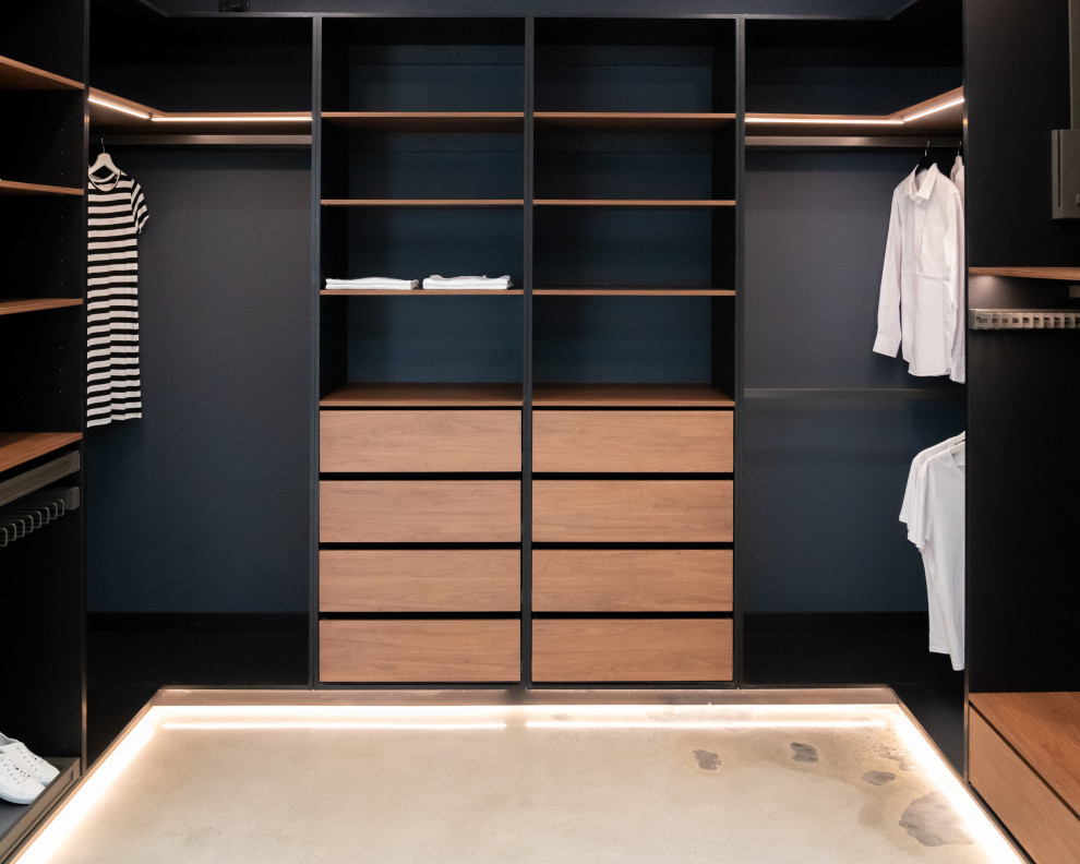 Imagen de armario vestidor actual de tamaño medio con armarios abiertos, puertas de armario de madera oscura y suelo de cemento