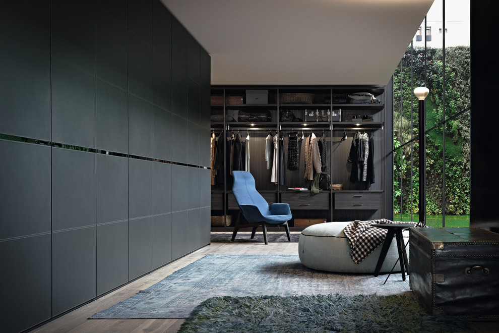 Diseño de armario vestidor unisex contemporáneo de tamaño medio con puertas de armario negras, suelo de madera en tonos medios y suelo marrón