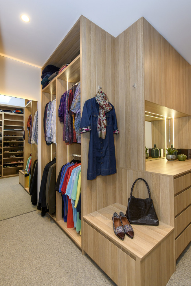 Modelo de armario vestidor unisex minimalista extra grande con armarios con paneles lisos, puertas de armario de madera clara, moqueta y suelo gris