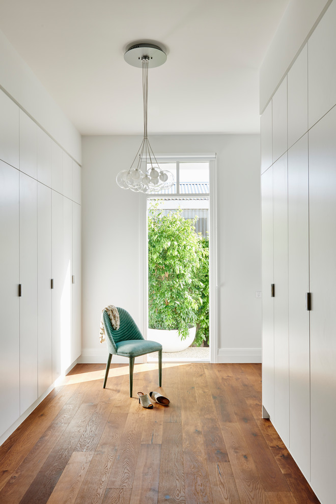 Inspiration for a contemporary women's dark wood floor and brown floor walk-in closet remodel in Geelong with flat-panel cabinets and white cabinets