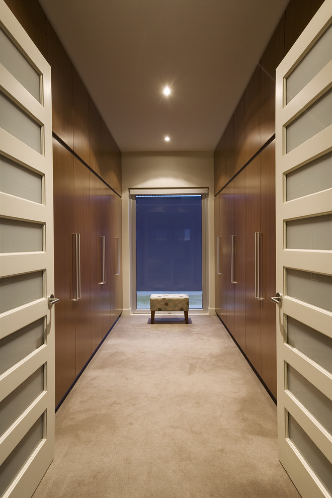 This is an example of a large modern gender neutral walk-in wardrobe in Sydney with flat-panel cabinets, medium wood cabinets and carpet.